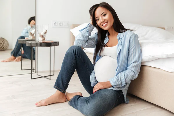 Glad gravid asiatisk kvinna lutande på en soffa sittande — Stockfoto