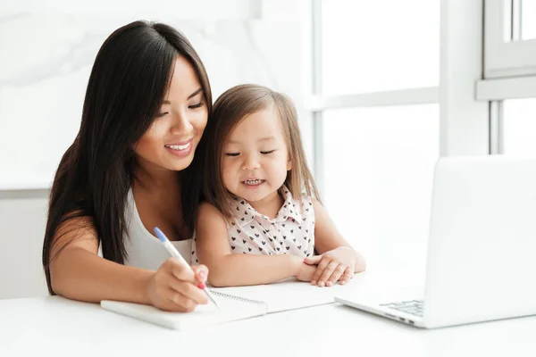 Mutter mit wenig süß asiatisch mädchen using laptop writing notes — Stockfoto