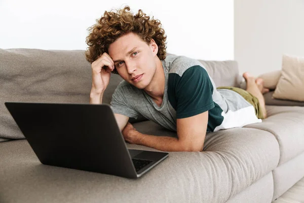 Bello uomo concentrato si trova sul divano utilizzando il computer portatile — Foto Stock