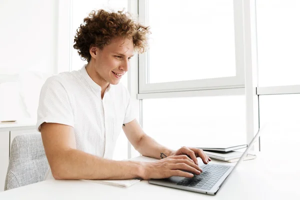 Ευτυχισμένος άνθρωπος που κάθεται στο τραπέζι κοντά στο παράθυρο χρησιμοποιώντας το φορητό υπολογιστή — Φωτογραφία Αρχείου