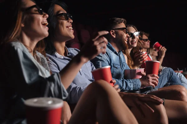 Happy friends sitting in cinema watch film eating popcorn.