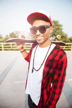 Genç koyu tenli adam kaykay tutan güneş gözlüğü takıyor