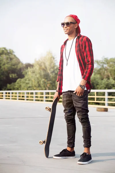 Junger dunkelhäutiger Mann mit Sonnenbrille und Skateboard — Stockfoto