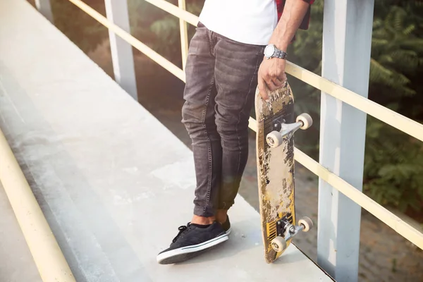 Foto ritagliata di giovane uomo dalla pelle scura in possesso di skateboard — Foto Stock