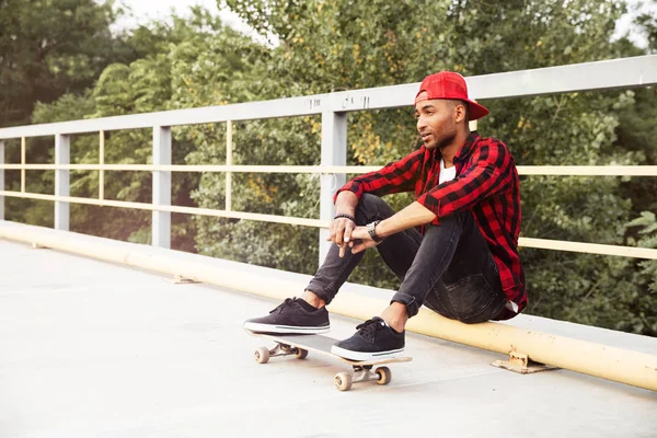 Donkere gevilde jongeman zit met zijn skateboard — Stockfoto