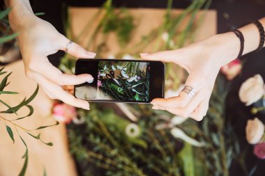Smartphone ve çiçek fotoğraflarını alarak masada tutarak çiçekçi