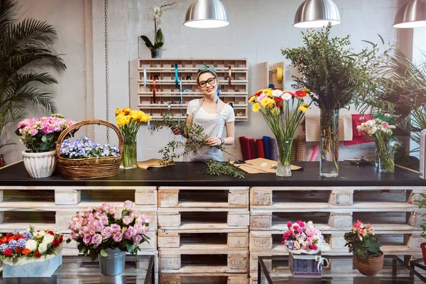 Щаслива красива молода жінка-флорист стоїть у квітковому магазині — стокове фото