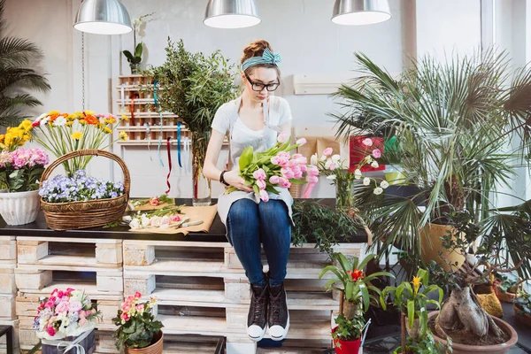 Mulher florista sentado e organizando tulipas rosa na loja de flores — Fotografia de Stock