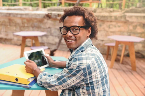 Wesoły Afryki młody człowiek w okularach, uśmiechając się i za pomocą tabletu — Zdjęcie stockowe