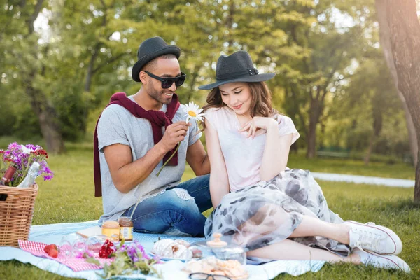 Sonriente joven dando flores a su novia en el picnic — Foto de Stock