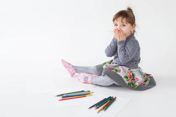 Портрет маленькой возбужденной девочки, сидящей и играющей цветными карандашами — стоковое фото