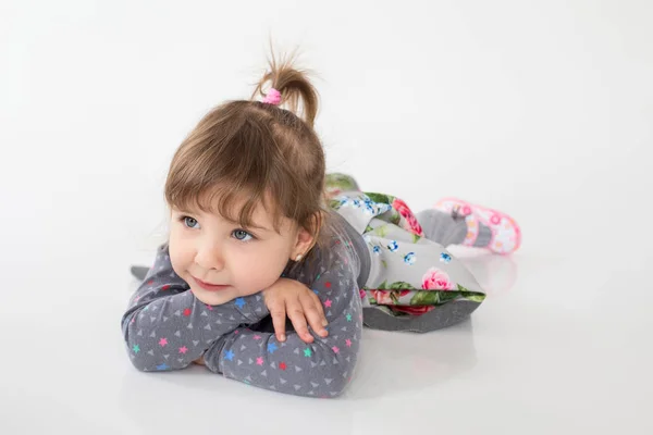 Улыбающаяся маленькая девочка лежит на полу на белом фоне — стоковое фото