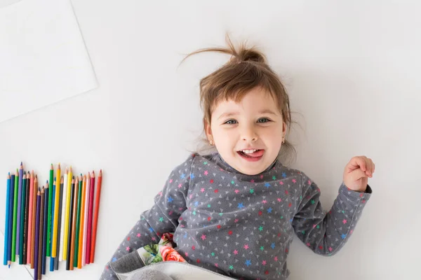 Fröhliches kleines Mädchen liegt neben vielen Buntstiften — Stockfoto