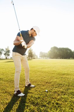 Genç erkek golfçü bir sopayla topa vuruyor