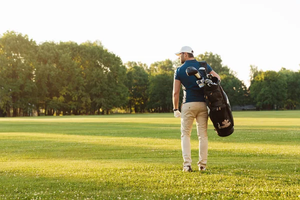 Visão traseira do jovem em cap carregando saco de golfe — Fotografia de Stock