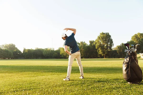 Joven golfista masculino estirando los músculos antes de comenzar el juego —  Fotos de Stock