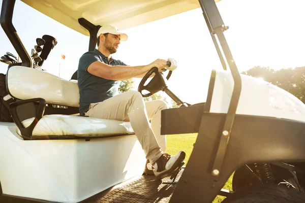Male golfer driving a cart with golf clubs