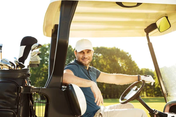 Bir golf arabası içinde oturan genç erkek golfçü gülümseyen