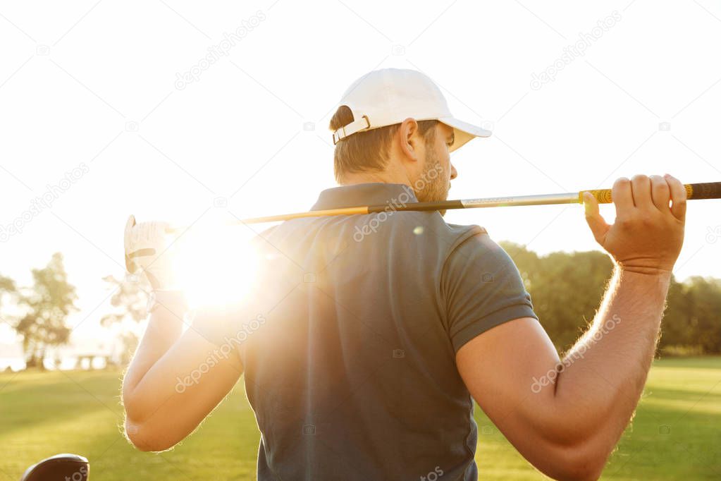 Back view of a young man carrying golf club