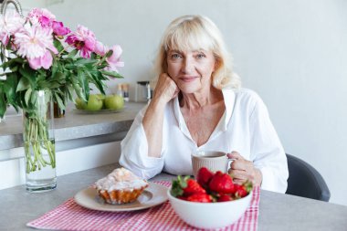Cupcake bir masada eğilerek gülümseyen Olgun kadın