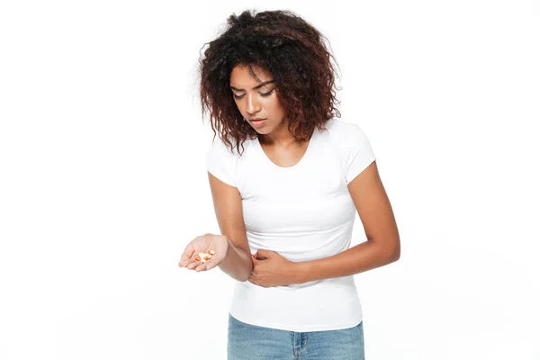 Sad young african lady holding pills with painful feelings.