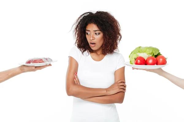 肉と野菜の間を選択する混乱している若いアフリカ女性. — ストック写真