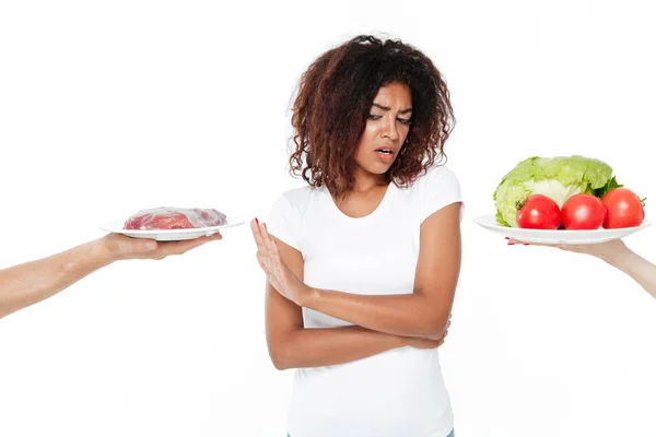 Confus jeune femme africaine choisir entre la viande et les légumes . — Photo