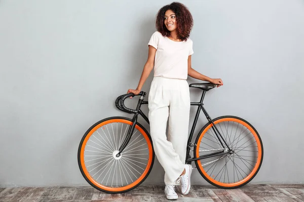 Imagem de comprimento total da mulher africana sorridente posando com bicicleta — Fotografia de Stock