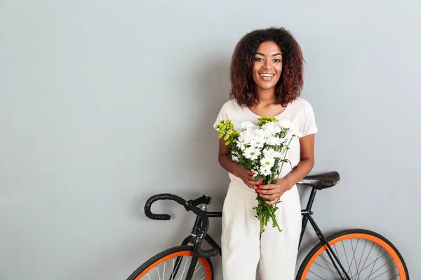 Hübsche lächelnde Afrikanerin posiert mit Fahrrad und Blumen — Stockfoto