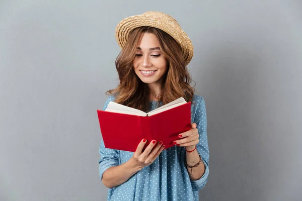 Mujer bonita de pie sobre la pared gris con sombrero libro de lectura . —  Fotos de Stock