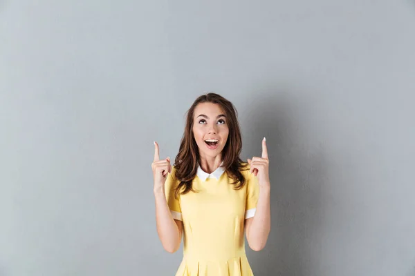 Garota sorridente excitada de pé e apontando o dedo para cima — Fotografia de Stock