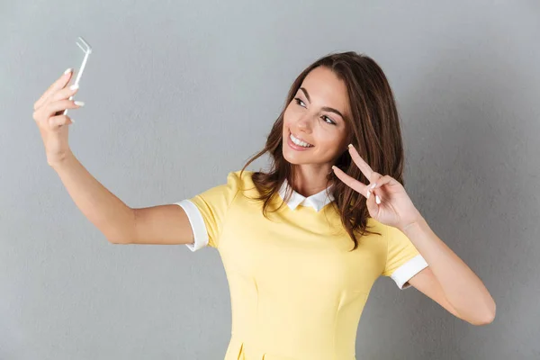 Sonriente chica bonita mostrando gesto de paz mientras se toma una selfie — Foto de Stock