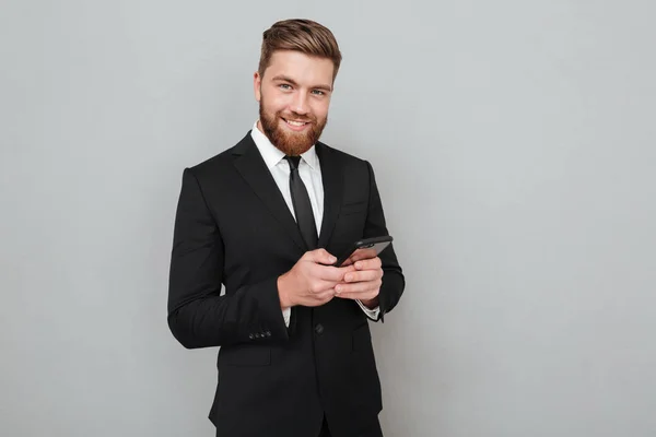 Sonriente hombre barbudo en traje usando su teléfono inteligente — Foto de Stock