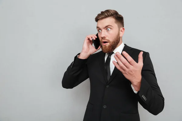 Sorprendido hombre barbudo hablando en su teléfono inteligente y mirando hacia otro lado — Foto de Stock