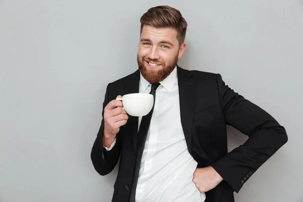 Sonriente hombre barbudo fresco en traje sosteniendo taza de café —  Fotos de Stock