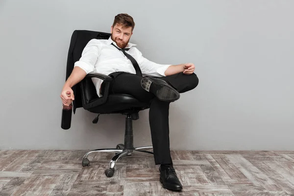 Счастливый пьяный бизнесмен сидит в офисном кресле с бутылкой — стоковое фото