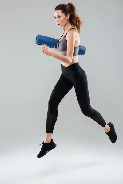 Ganska friska idrottskvinna holding fitness mat medan hoppning — Stockfoto