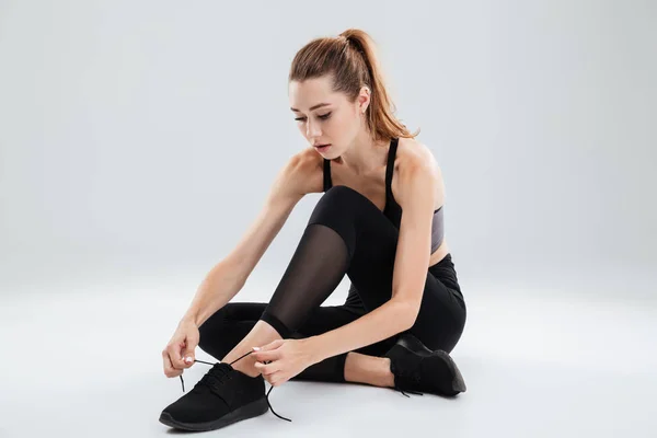 Молодая спортсменка сидит и завязывает шнурки — стоковое фото