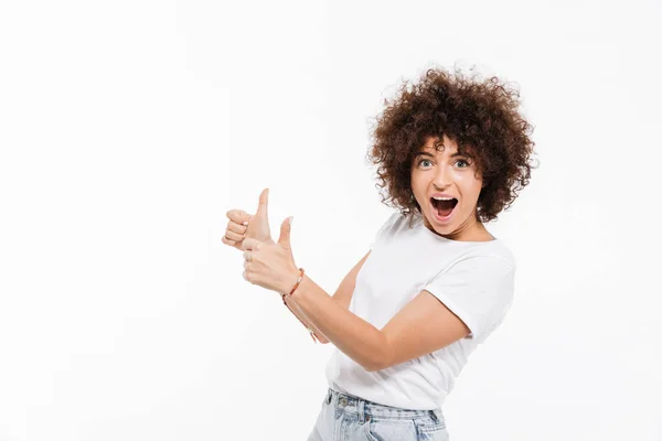 Lycklig kvinna med lockigt hår pekar två tummen upp åt sidan — Stockfoto