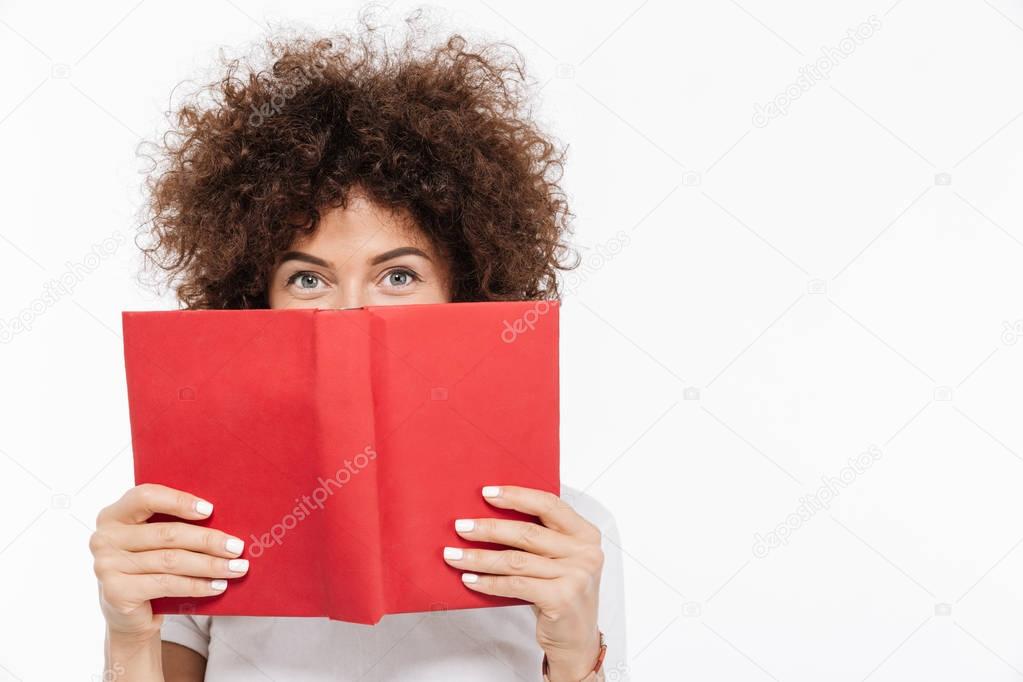 Pretty woman with curly hair peeking out of a book