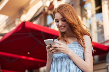 Cep telefonu kullaranarak gülümseyen güzel kızıl saçlı kız