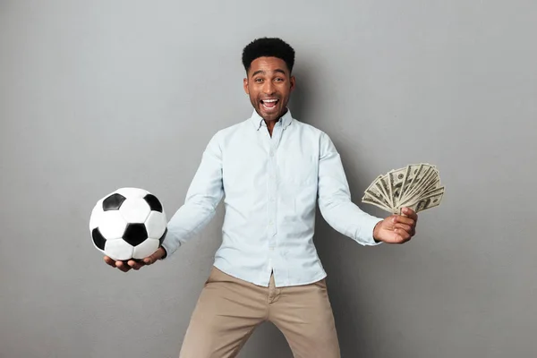 Happy smiling african man holding football and money banknotes — Stock Photo, Image