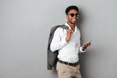 Gülümseyen Afrika adam ceket omzunun üzerinden tutan güneş gözlüğü