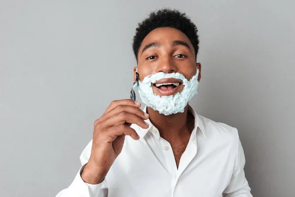 Young african man in shirt shaving with a razor