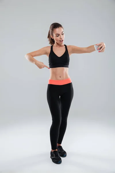 Obraz pełnej długości szczęśliwy fitness Kobieta wskazując na mięśnie brzucha — Zdjęcie stockowe