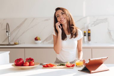 Pişirme sırasında cep telefonu üzerinde konuşurken gülümseyen genç kadın