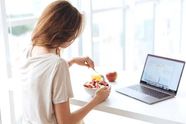 Vista posteriore della donna fare colazione e utilizzando il computer portatile — Foto Stock