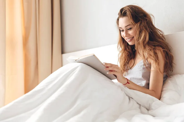 Alegre bella dama se encuentra en la cama en el interior libro de lectura . —  Fotos de Stock