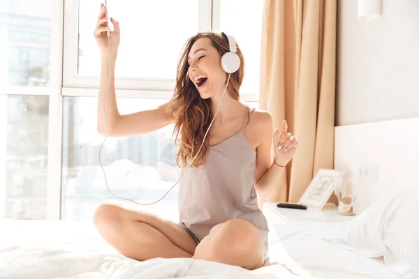 ベッドでヘッドフォンで音楽を聴く若い幸せな女 — ストック写真