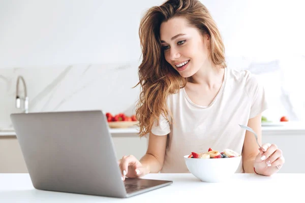 Mujer bonita charlando en el ordenador portátil y comiendo frutas — Foto de Stock